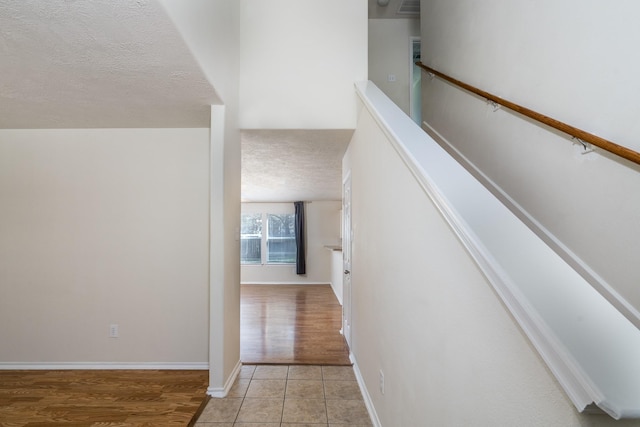 corridor featuring light tile patterned floors, baseboards, and a textured ceiling