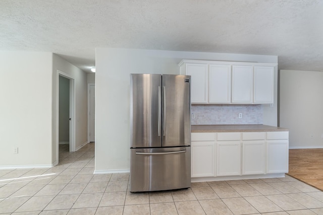 kitchen with light tile patterned floors, freestanding refrigerator, light countertops, white cabinetry, and backsplash