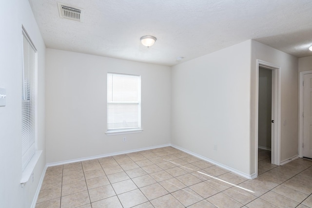 spare room featuring a textured ceiling, light tile patterned flooring, visible vents, and baseboards