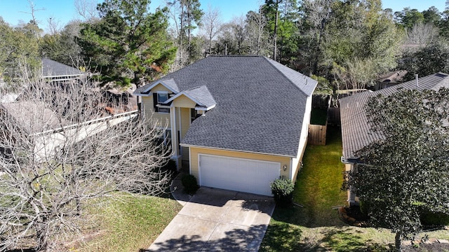 view of front of property featuring an attached garage, fence, concrete driveway, roof with shingles, and a front yard