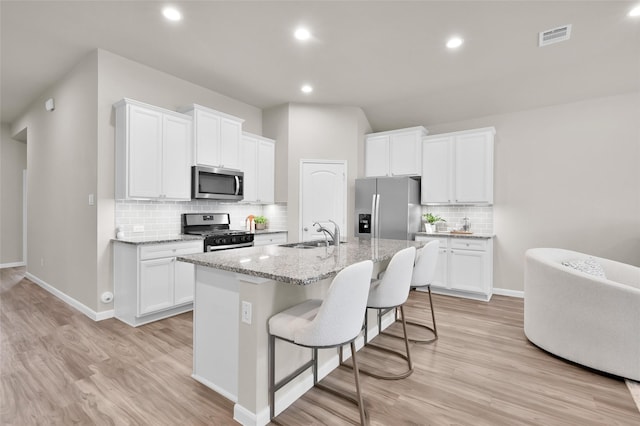 kitchen featuring light wood finished floors, a center island with sink, stainless steel appliances, white cabinetry, and a sink