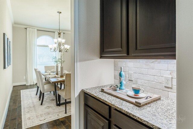 kitchen with dark wood-style flooring, dark brown cabinetry, light stone countertops, a chandelier, and decorative backsplash