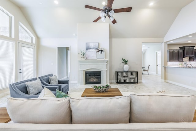 living area featuring high vaulted ceiling, a glass covered fireplace, a ceiling fan, baseboards, and recessed lighting