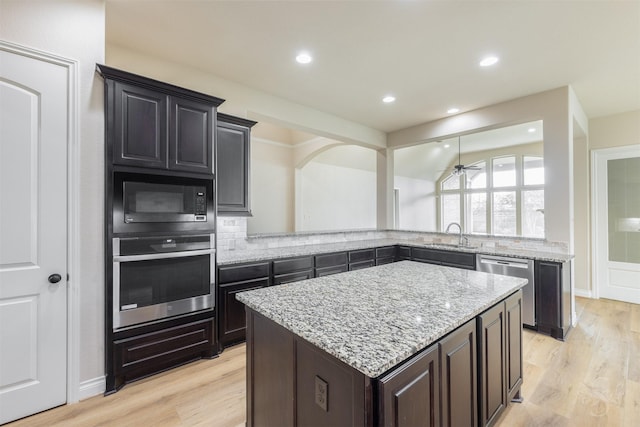 4903 Cancun Hills Ct, Fulshear, TX 77441 - kitchen with stainless steel appliances, light wood-style flooring, light stone counters, a center island, and backsplash