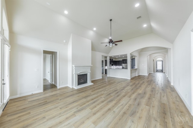 4903 Cancun Hills Ct, Fulshear, TX 77441 - unfurnished living room with ceiling fan, arched walkways, light wood-style flooring, high vaulted ceiling, and a fireplace with raised hearth
