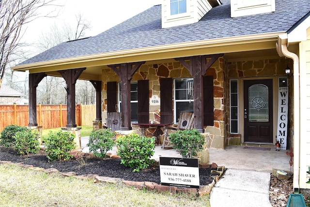 view of exterior entry with a shingled roof and fence