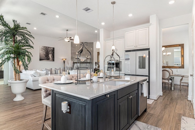 kitchen featuring visible vents, open floor plan, white cabinets, a sink, and wood finished floors