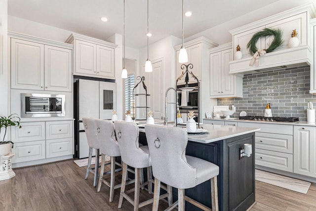 kitchen with light countertops, decorative backsplash, appliances with stainless steel finishes, wood finished floors, and a kitchen breakfast bar