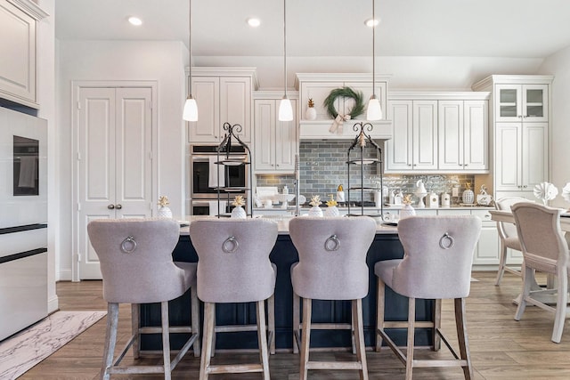 kitchen with a center island with sink, light wood-style flooring, a breakfast bar, light countertops, and stainless steel double oven