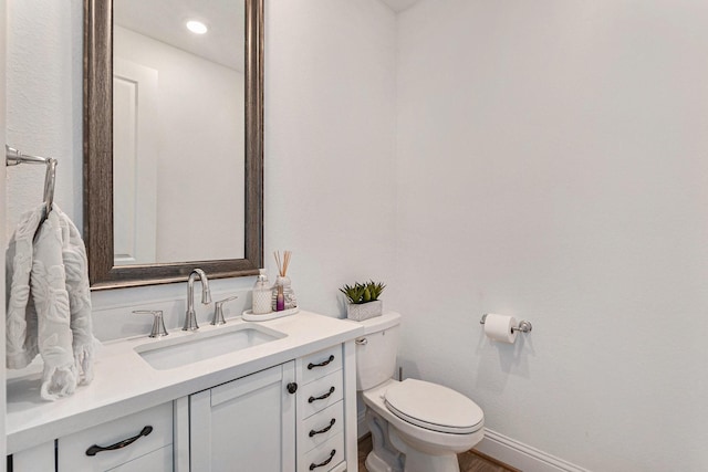 half bathroom with vanity, toilet, and baseboards