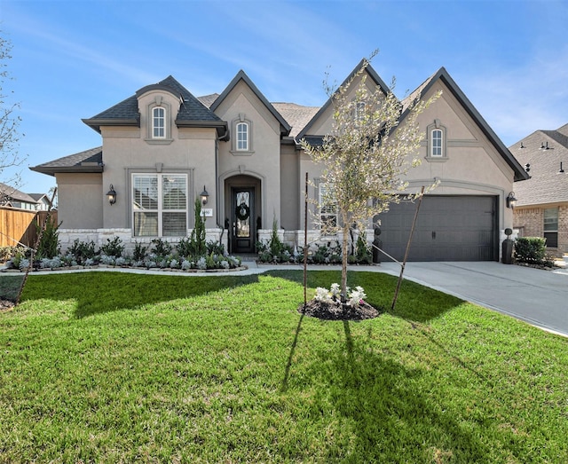 french country style house with a front yard, an attached garage, driveway, and stucco siding