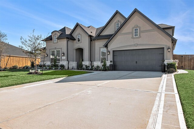 french country style house with concrete driveway, a front yard, fence, and stucco siding