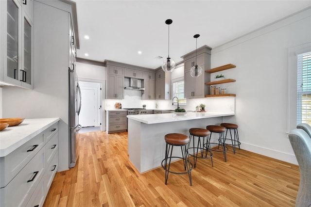 kitchen featuring tasteful backsplash, wall chimney exhaust hood, a breakfast bar area, a peninsula, and gray cabinetry