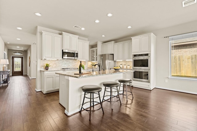 kitchen with light stone counters, dark wood-style flooring, visible vents, white cabinets, and appliances with stainless steel finishes