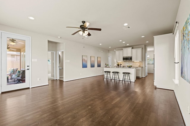 unfurnished living room with baseboards, visible vents, a ceiling fan, dark wood-type flooring, and recessed lighting