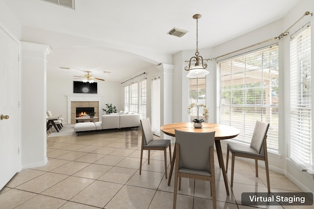 dining space featuring light tile patterned floors, arched walkways, a tile fireplace, visible vents, and a ceiling fan