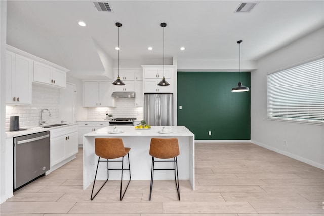 kitchen featuring visible vents, a kitchen island, appliances with stainless steel finishes, under cabinet range hood, and a sink