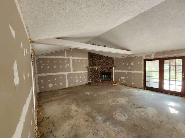 unfurnished living room with vaulted ceiling, concrete floors, a stone fireplace, and a textured ceiling