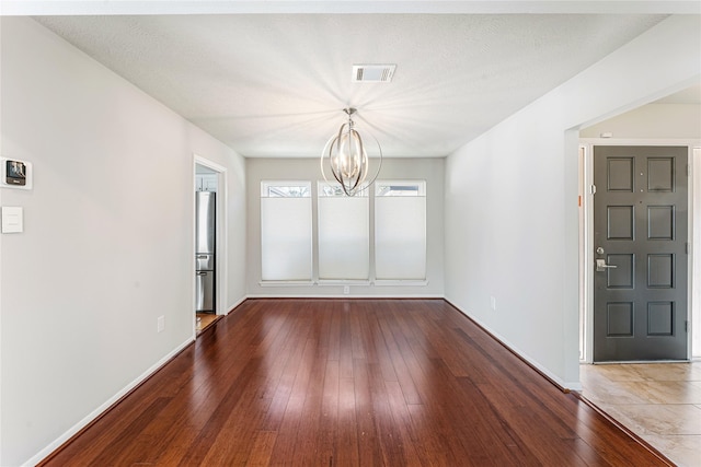 unfurnished dining area with an inviting chandelier, wood-type flooring, visible vents, and baseboards