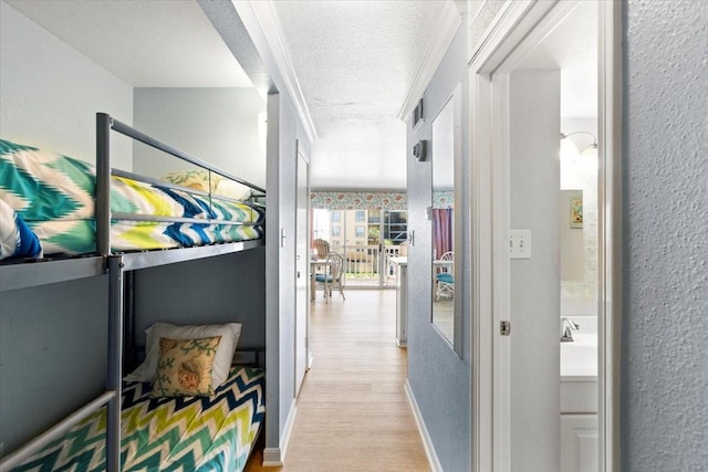 hallway featuring crown molding, light wood finished floors, a textured wall, a textured ceiling, and baseboards