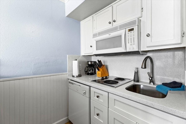 kitchen featuring a wainscoted wall, white appliances, a sink, white cabinetry, and light countertops