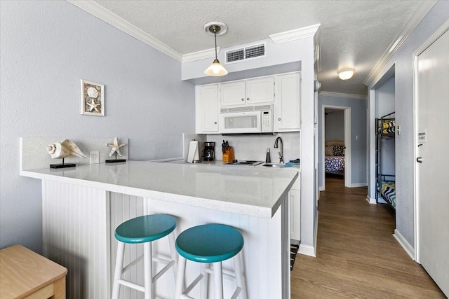 kitchen featuring visible vents, white microwave, a peninsula, crown molding, and white cabinetry