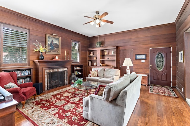 living area featuring ceiling fan, a fireplace, wood walls, and wood finished floors