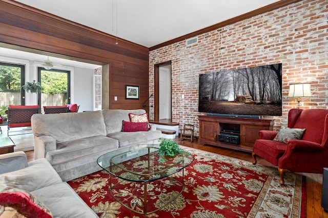 living area with wood walls, brick wall, visible vents, and wood finished floors