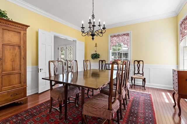 dining space with wainscoting, a notable chandelier, crown molding, and hardwood / wood-style floors