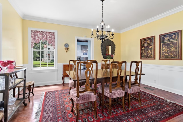 dining area featuring a wainscoted wall, dark wood-type flooring, crown molding, and an inviting chandelier