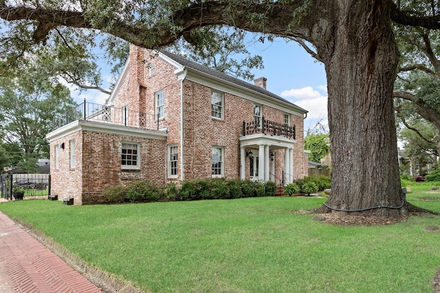 view of front facade with brick siding, a chimney, a front yard, and a balcony