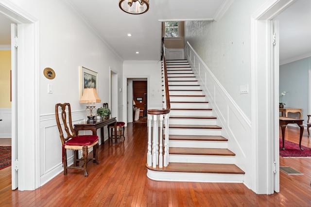 stairs featuring visible vents, a wainscoted wall, wood-type flooring, crown molding, and a decorative wall