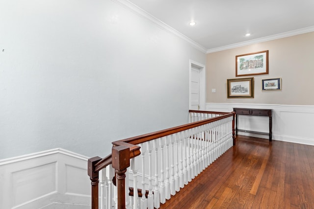 hallway with a wainscoted wall, wood-type flooring, ornamental molding, and an upstairs landing