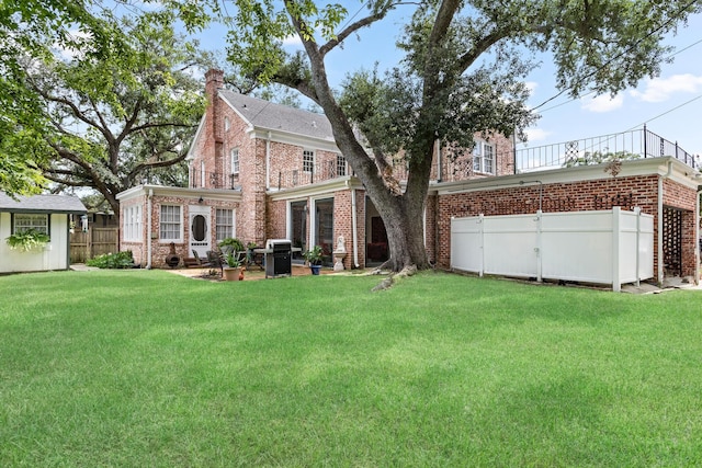 back of house featuring a lawn, a chimney, fence, an outdoor structure, and brick siding