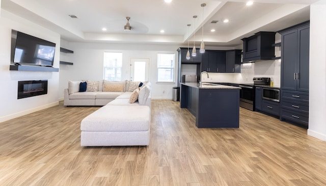 living area featuring baseboards, visible vents, a glass covered fireplace, a raised ceiling, and light wood-type flooring