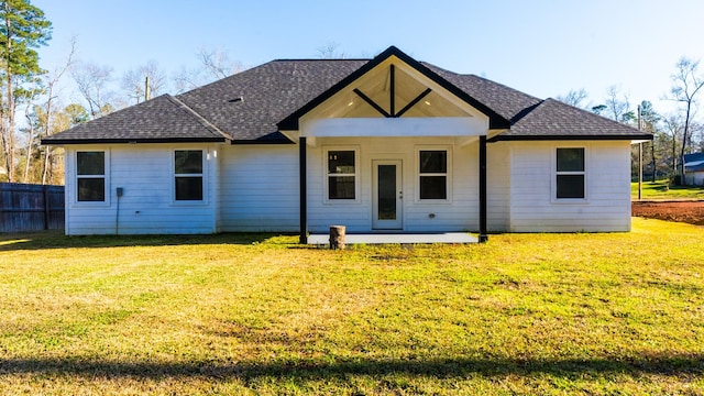 rear view of property featuring a patio, a yard, fence, and a shingled roof