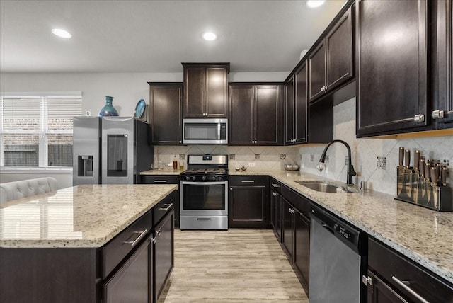 kitchen featuring stainless steel appliances, a sink, light wood-type flooring, light stone countertops, and tasteful backsplash