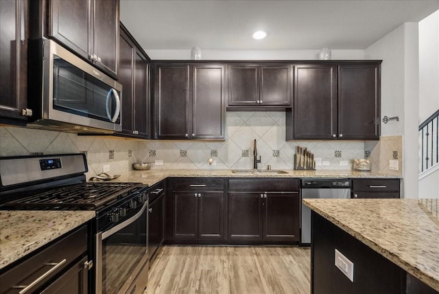 kitchen with light stone counters, stainless steel appliances, a sink, backsplash, and light wood finished floors