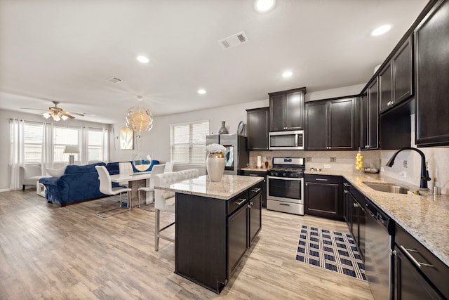 kitchen with visible vents, a kitchen island, stainless steel appliances, a kitchen bar, and a sink