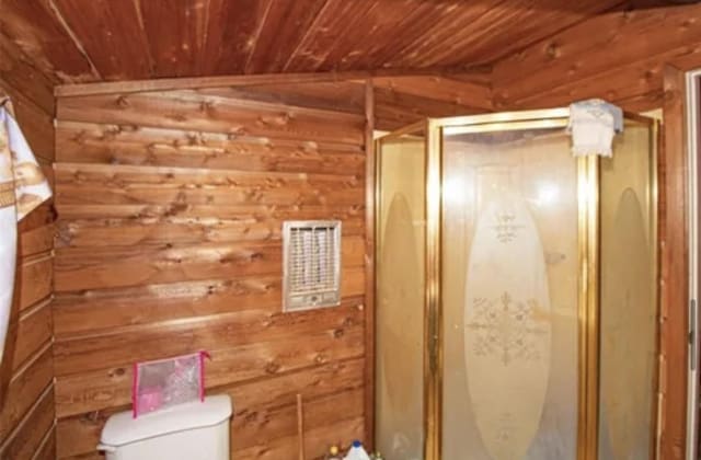 bathroom with toilet, wood ceiling, vaulted ceiling, wood walls, and a shower stall