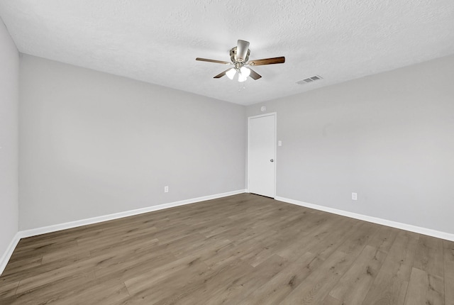 empty room featuring a ceiling fan, wood finished floors, visible vents, and baseboards