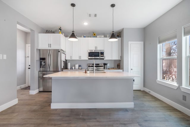 kitchen with a center island with sink, visible vents, baseboards, appliances with stainless steel finishes, and white cabinetry