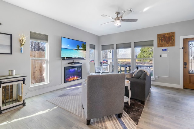 living room with a glass covered fireplace, ceiling fan, baseboards, and wood finished floors