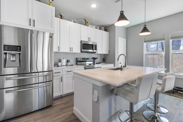 kitchen featuring appliances with stainless steel finishes, white cabinets, a sink, and an island with sink