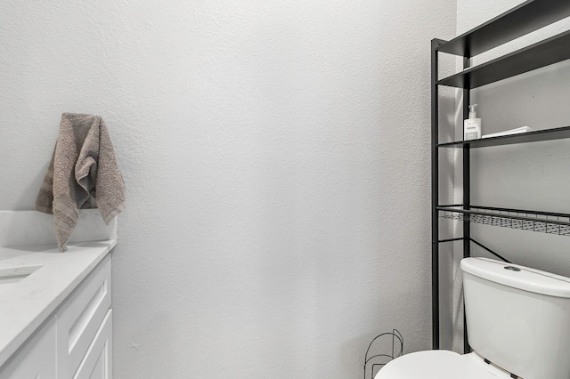 bathroom with a textured wall, vanity, and toilet