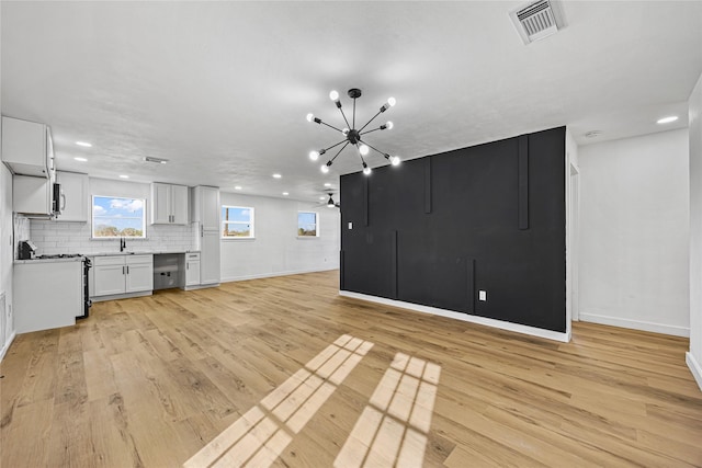 unfurnished living room with light wood-type flooring, visible vents, baseboards, and a sink