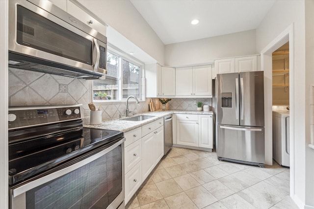 kitchen with stainless steel appliances, white cabinets, a sink, light stone countertops, and washer / dryer