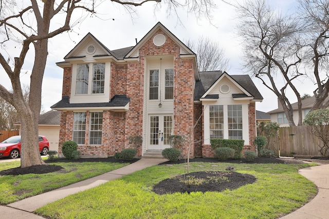 traditional-style home featuring a front yard, french doors, brick siding, and fence