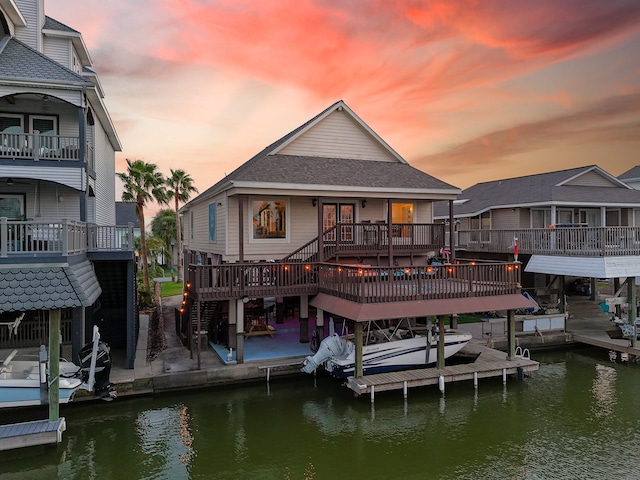 back of house at dusk featuring a patio, a shingled roof, a deck with water view, and boat lift