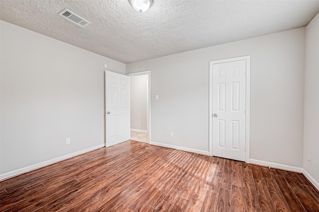 empty room with a textured ceiling, wood finished floors, visible vents, and baseboards